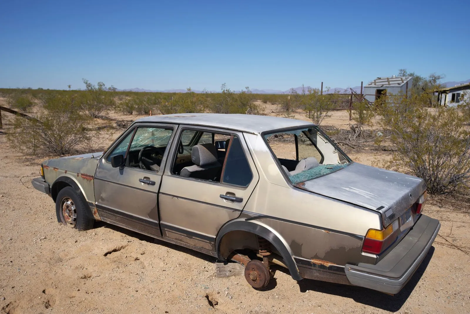 Old sedan sitting on bare ground with one wheel missing
