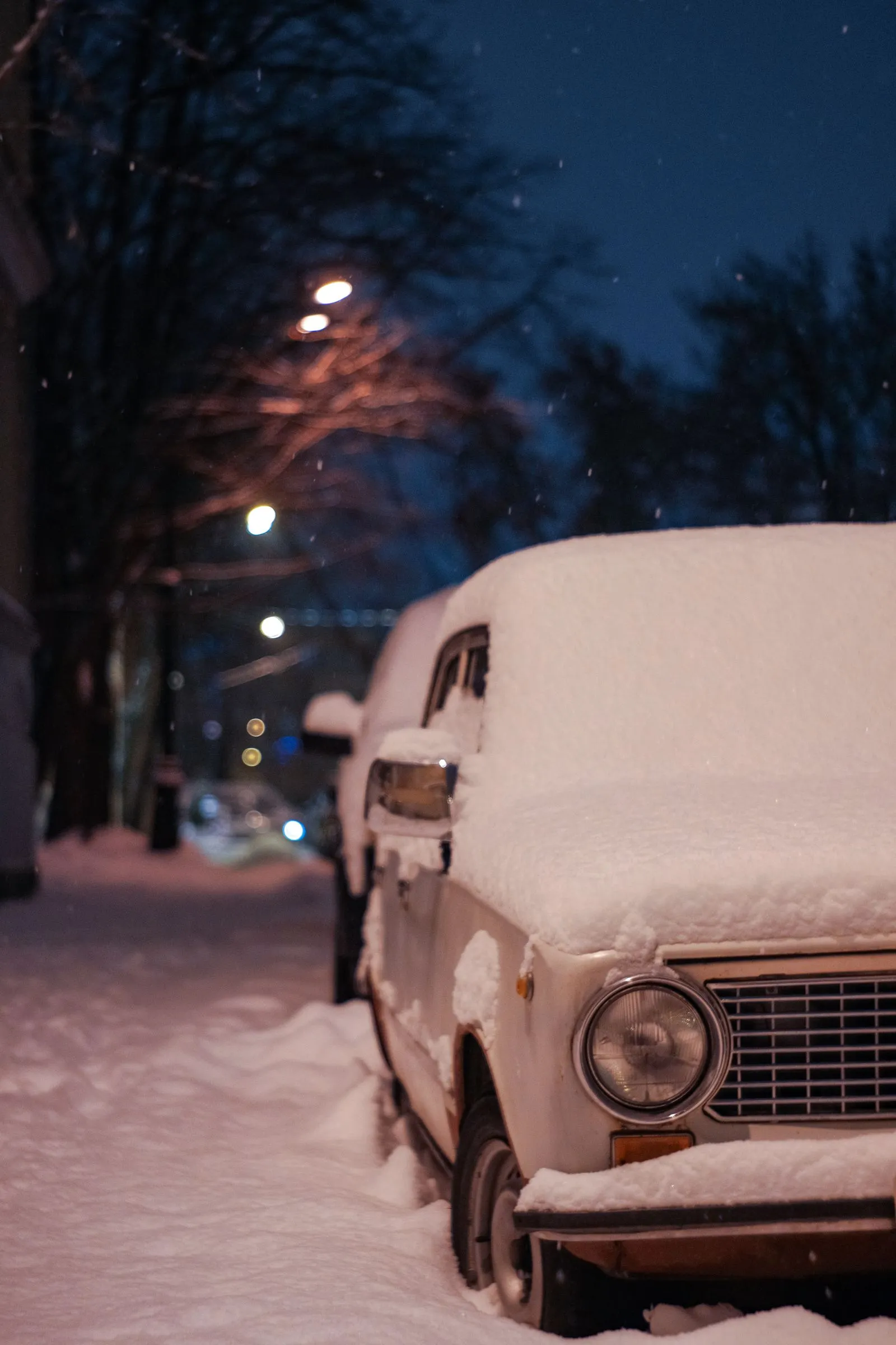 Old sedan buried in snow at the curb on a winter night