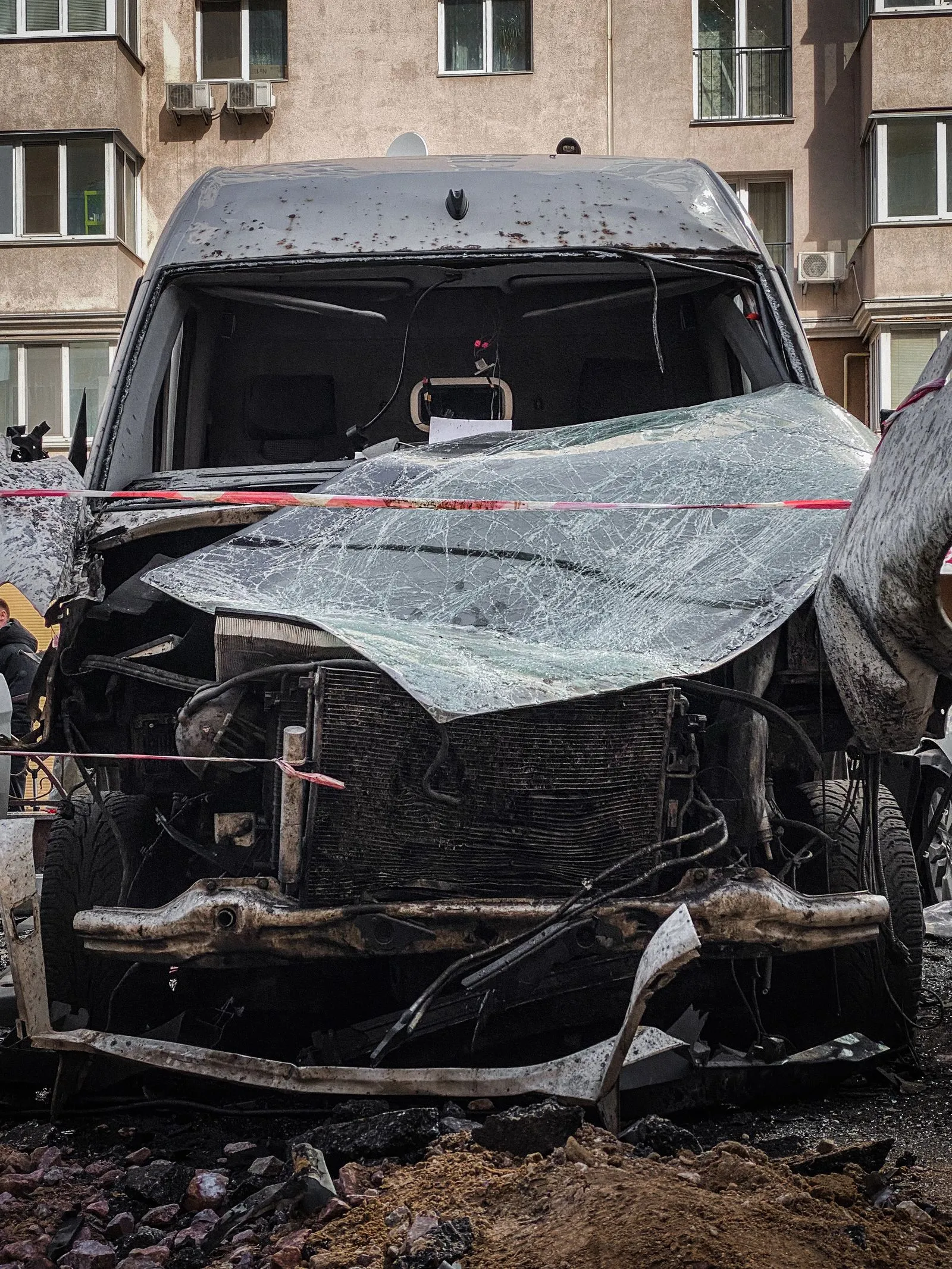 Van with its front end torn open after a crash, parked by an apartment building